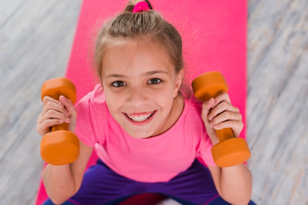 An overhead view of smiling girl holding dumbbell in hands