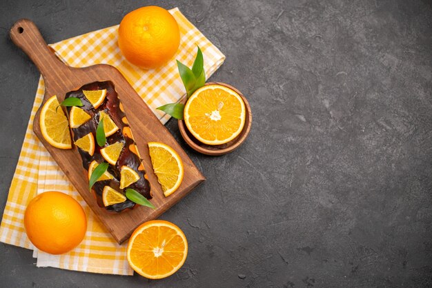 Overhead view of soft cakes and cut oranges with leaves on dark table