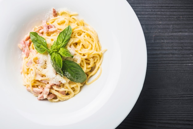 An overhead view of spaghetti with basil leaf and cheese toppings