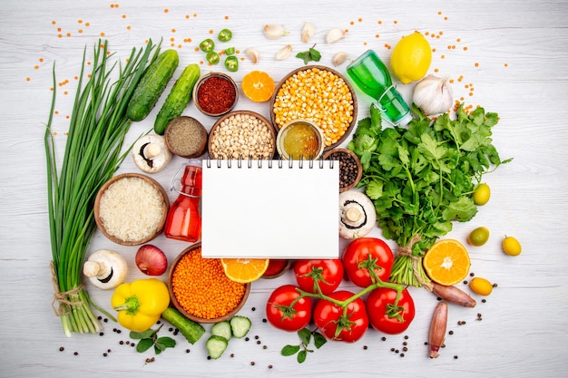 Free Photo overhead view of a spiral notebook on fresh vegetables lemon corn kernels lemon fallen oil bottle honey on white background