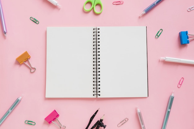 Free photo overhead view of spiral notepad surrounded by various stationeries on pink backdrop