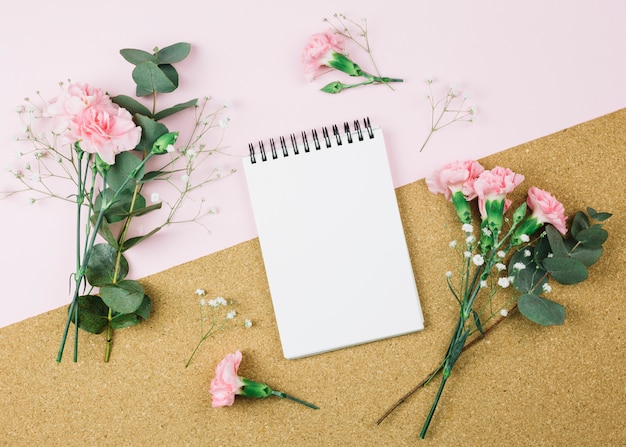 Free photo an overhead view of spiral notepad surrounded with gypsophila and carnation flowers on dual pink and cardboard background