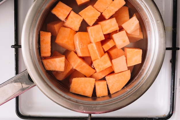 An overhead view of sweet potatoes slice boiling in the metal saucepan on gas