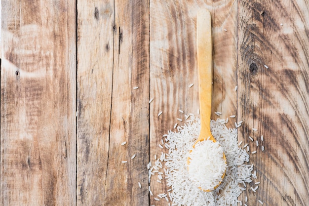 Free photo overhead view of tasty raw rice spilling out of wooden spoon with space for text