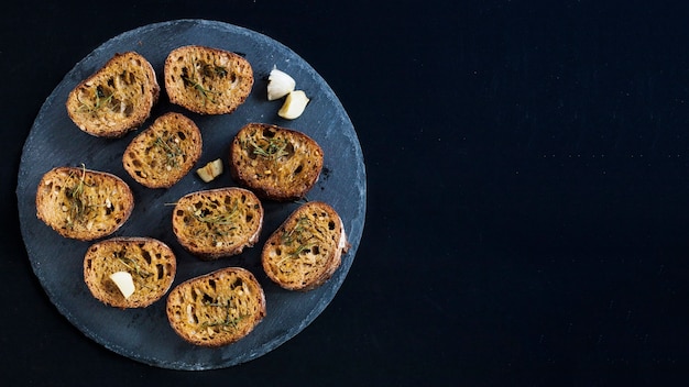 Free photo an overhead view of toast with rosemary toppings on round slate against black background