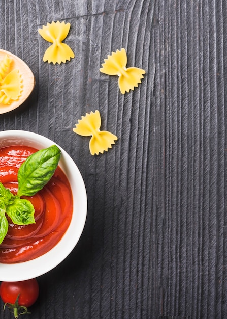 Free photo an overhead view of tomato sauce with uncooked pasta on black wooden backdrop