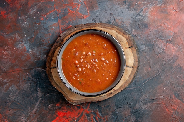 Free photo overhead view of tomato soup in a blue bowl on a brown wooden tray on mixed color table