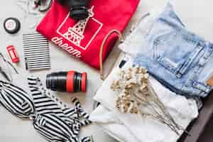 Free photo overhead view of travelling bag with female outfits and flowers