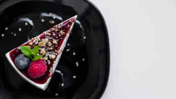 Free photo an overhead view of triangular cheesecake with raspberry; blueberry and mints on black ceramic plate against white background