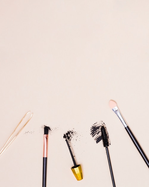 Free photo an overhead view of tweezers; makeup brush and mascara brush isolated on beige background