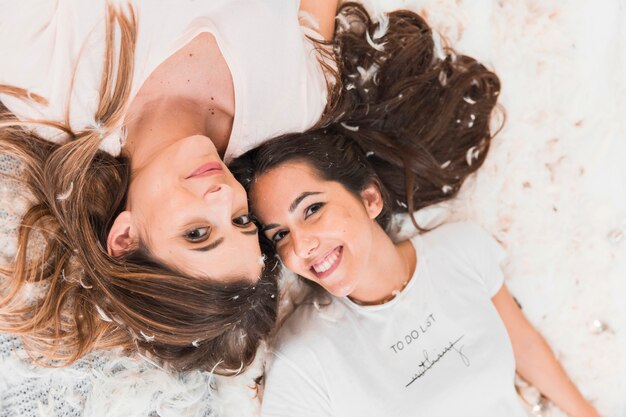 An overhead view of two smiling women lying over soft feathers