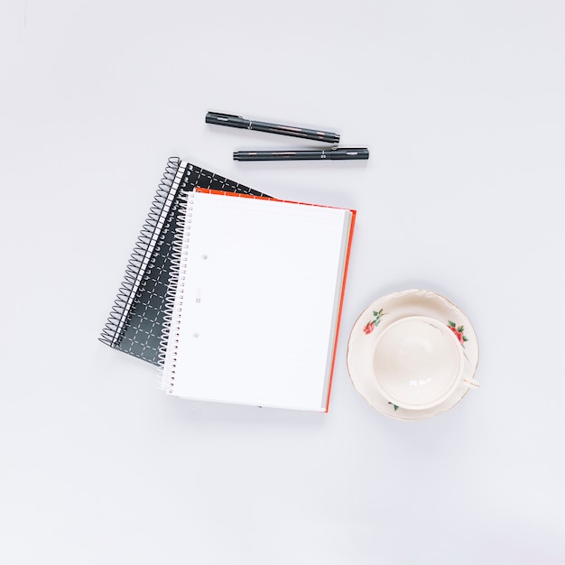 Free photo overhead view of two spiral notebook; pen and empty cup on white background