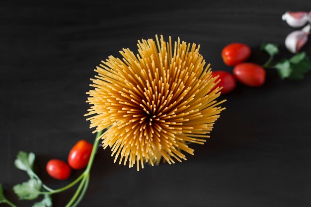 An overhead view of uncooked pasta spaghetti with ingredients against black background