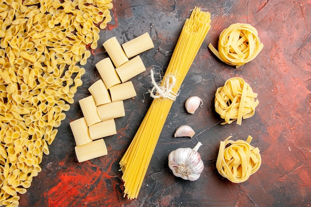 Overhead view of uncooked pasta in various forms and garlic on black table