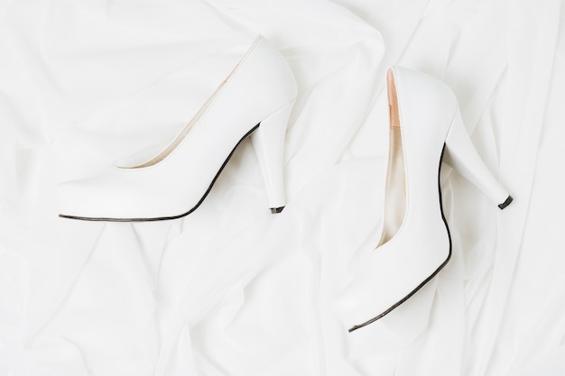 An overhead view of wedding white high heels on white cloth