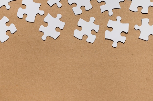 Overhead view of white puzzle pieces on brown paper textured