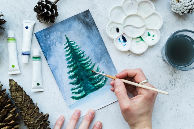 Free Photo an overhead view of a woman's hand painting christmas tree on canvas