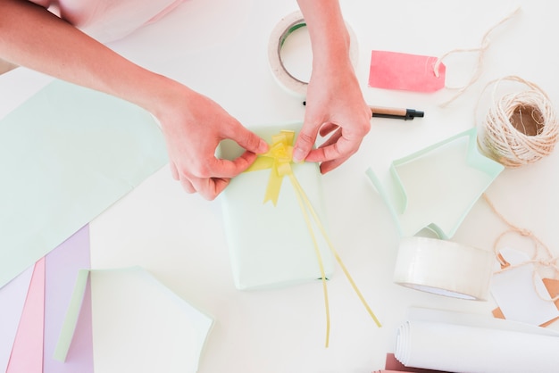 Free photo an overhead view of woman sticking yellow ribbon on wrapped gift box