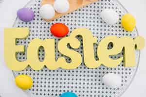 Free photo an overhead view of yellow easter word with colorful eggs on white round table