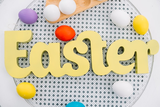 An overhead view of yellow easter word with colorful eggs on white round table