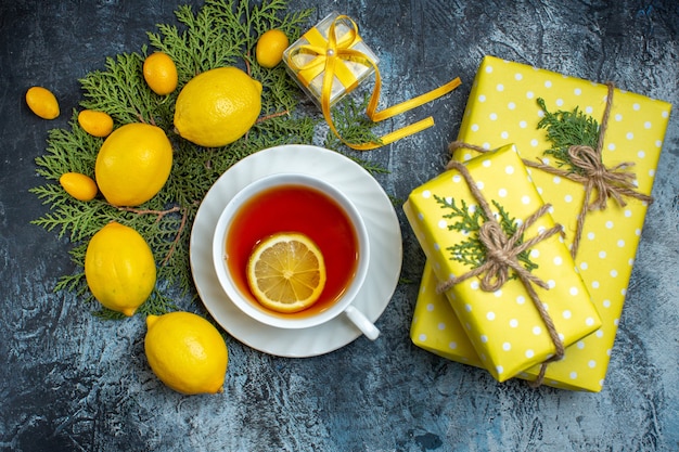 Free photo overhead view of yellow gift boxes and a cup of black tea with lemon and collection of natural organic fresh citrus fruits on fir branches on dark background