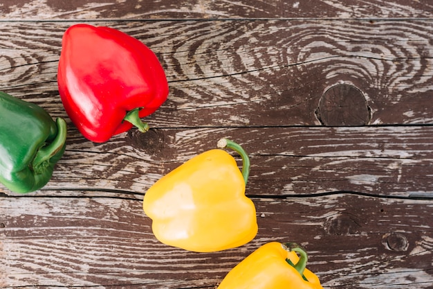 An overhead view of yellow; green and red bell peppers on wooden texture surface