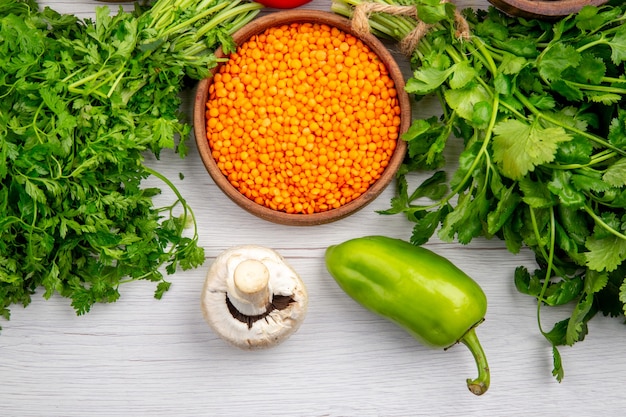 Overhead view of yellow lentil bundle of greens mushrooms on white table