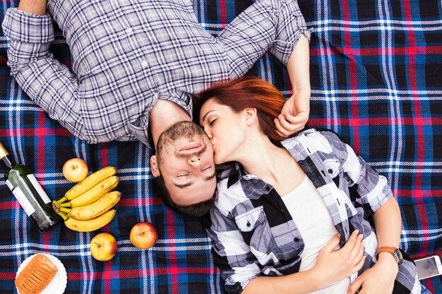 An overhead view of young woman kissing her boyfriend lying on blanket