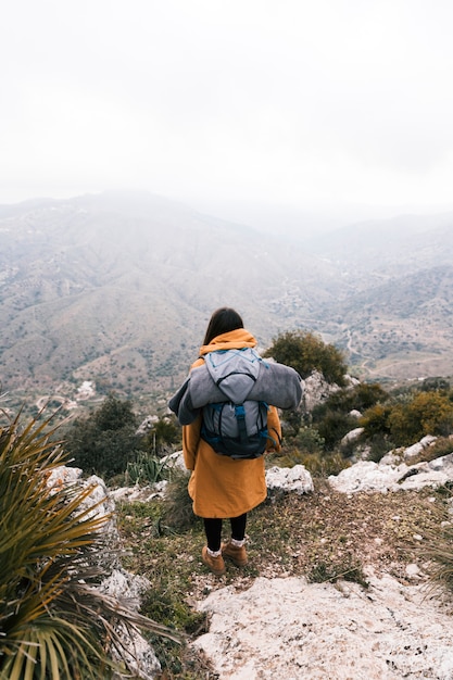 Free photo an overhead view of a young woman with her backpack overlooking the mountain