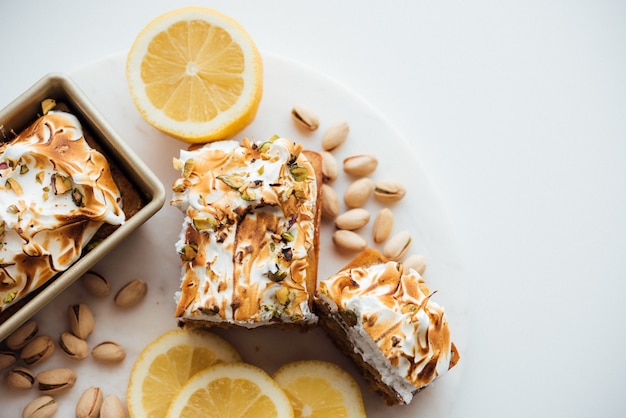 Overhead wide shot of tasty cake dessert with nuts and lemons on a white plate and white background