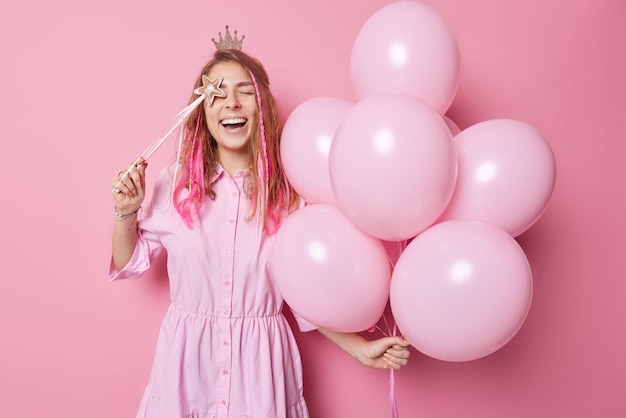 Free Photo overjoyed glad young woman poses with bunch of inflated balloons and magic wand has fun on party foolishes around isolated over pink background enjoys holiday people and celebration concept