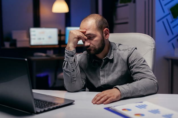 Overworked businessman sleeping resting his head on his hand. Workaholic employee falling asleep because of working late at night alone in the office for important company project.