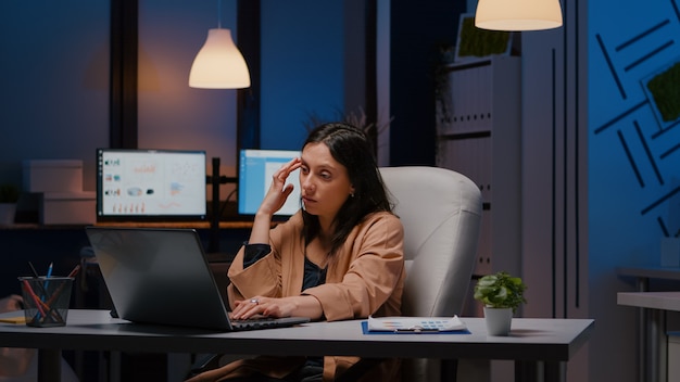 Free photo overworked exhausted businesswoman working in startup office checking management strategy on laptop late at night