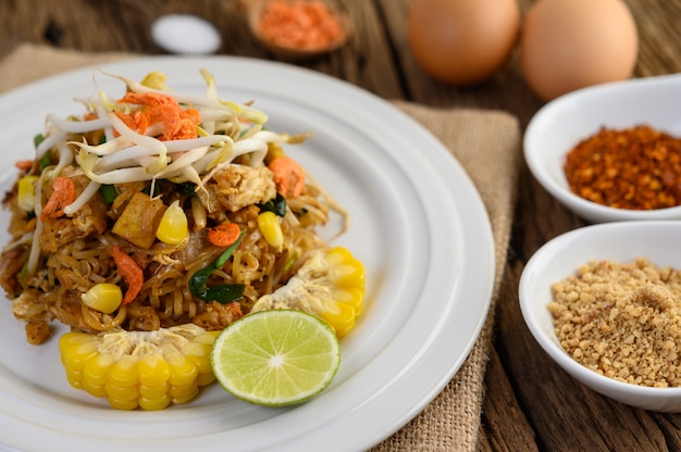 Pad Thai in a white plate with lemon, eggs and seasoning on a wooden table.