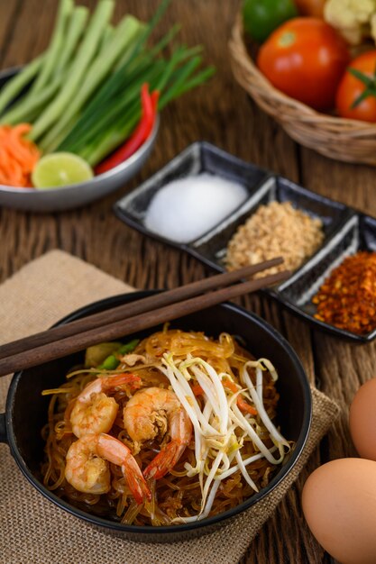 Padthai shrimp in a black bowl with eggs and Seasoning on wooden table.