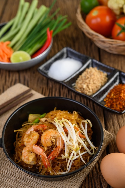 Padthai shrimp in a black bowl with eggs and Seasoning on wooden table.