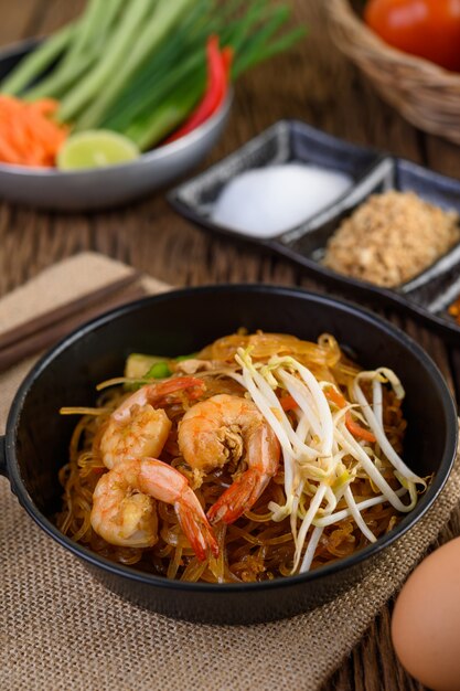 Padthai shrimp in a black bowl with eggs and Seasoning on wooden table.