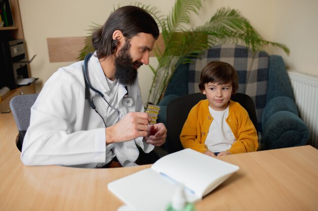 Paediatrician doctor examining a child in comfortabe medical office. Healthcare, childhood, medicine, protection and prevention concept. Little boy trust to doctor and feels calm, positive emotions.