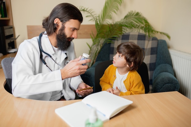 Paediatrician doctor examining a child in comfortabe medical office. Healthcare, childhood, medicine, protection and prevention concept. Little boy trust to doctor and feels calm, positive emotions.