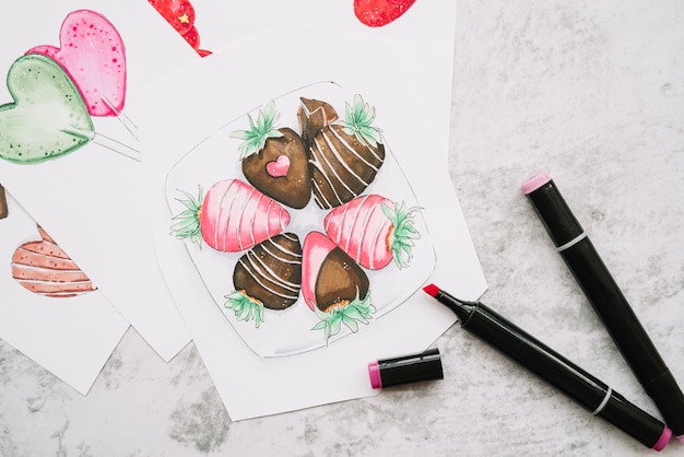 Free photo painted hearts and strawberries on paper near markers