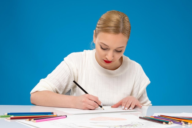 Free photo painter lovely young pretty girl in red lipstick drawing something on the paper with black pencil