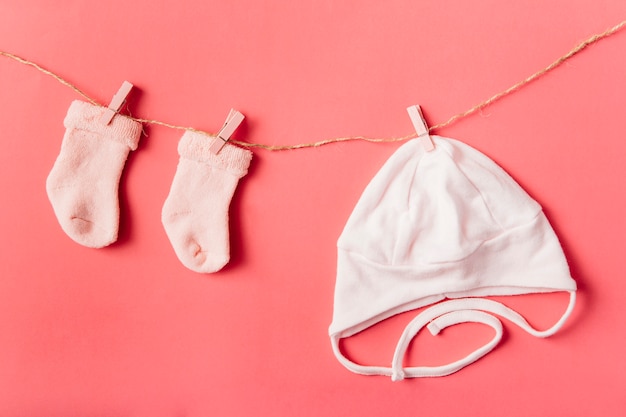 Free photo pair of baby's sock and cap hanging with clothespin on string against colored backdrop