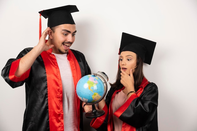 Free Photo pair of happy students in gown looking at globe on white.