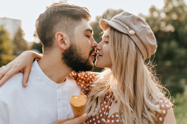 Pair of lovers kisses with closed eyes. Guy and girl in summer clothes holding ice cream.