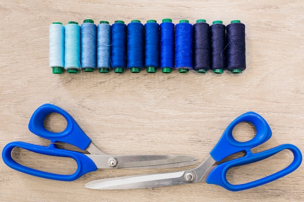 Pair of scissors and threads arranged in a row on wooden background