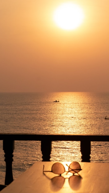 Pair of sunglasses on the table by the sea during sunset