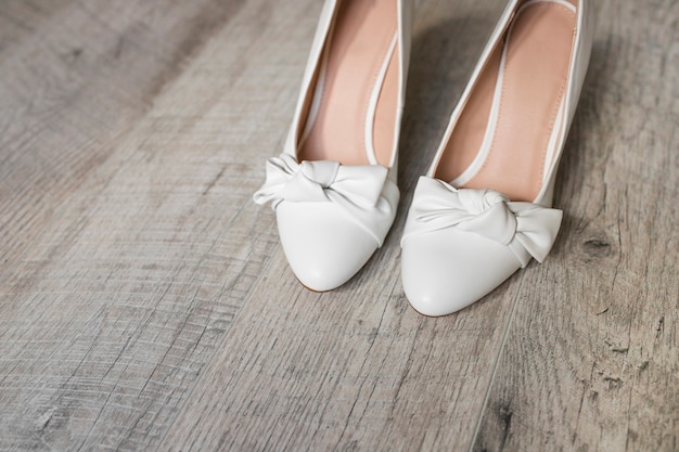 Pair of white dress shoes with bow on wooden textured background