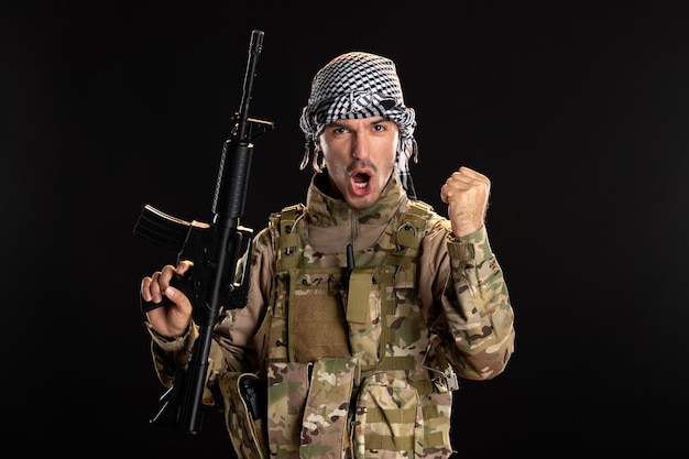 Free Photo palestinian serviceman in military uniform with rifle on dark wall