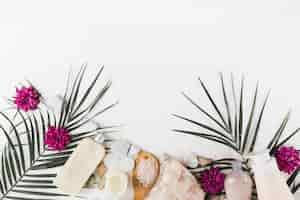 Free photo palm leaves; flower; body scrub; salt; spa stones on white background