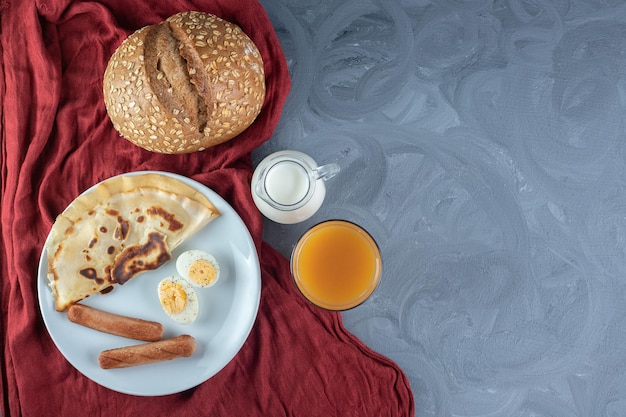 Free Photo pancake, sausages and slices of boiled egg next to milk, juice and bread on marble table.